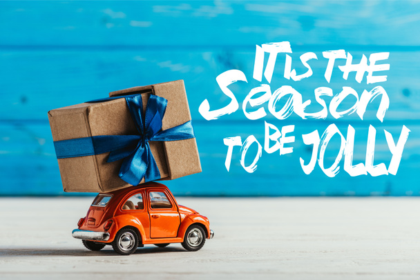 primer plano de coche de juguete con caja de regalo sobre fondo de madera azul con inspiración "es la temporada para ser alegre"
 - Foto, imagen