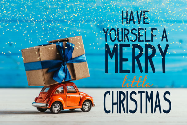 close-up shot of toy car with gift box on blue wooden background with "have yourself a merry little christmas" inspiration - Foto, immagini