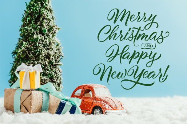 赤グッズ プレゼントとクリスマス ツリーの雪の上に立って車のクローズ アップ ショット コットン青色の背景に「メリー クリスマスと新年あけましておめでとうございます」の文字 - 写真・画像