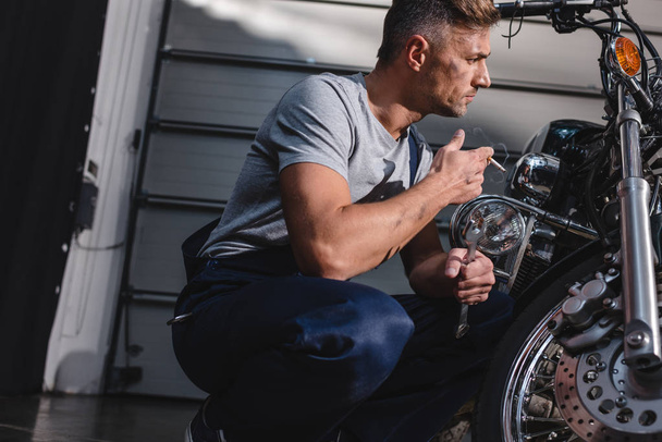 mechanic checking motorcycle front wheel and smoking in garage - 写真・画像