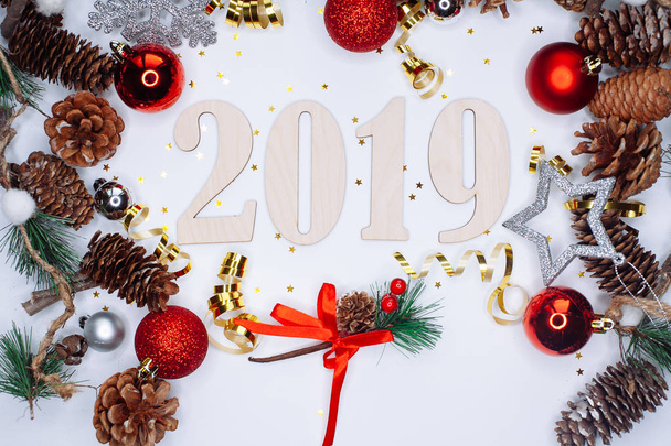 Christmas and New Year composition. 2019 simbols and fir branches with cones and christmas balls in silver and red colours on white background. Flat lay, top view, copy space for text - Photo, image