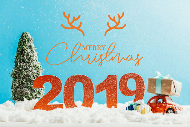 big red 2019 numbers with toy car, gifts and christmas tree on snow with "merry christmas" lettering - Fotó, kép