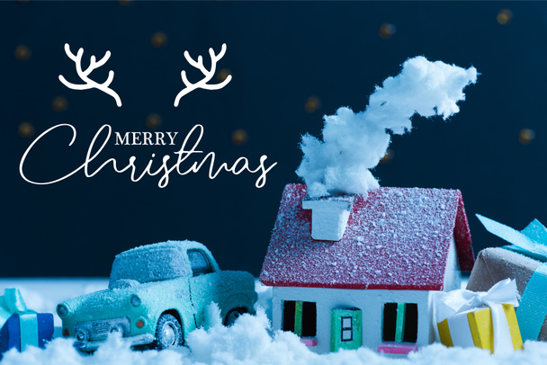 Nahaufnahme von Miniatur-Auto mit Weihnachtsgeschenken und schneebedecktem Haus in der Nacht, mit "Frohe Weihnachten" -Schriftzug mit Hirschhörnern - Foto, Bild