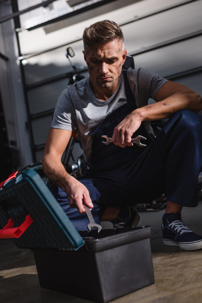 mecánico sentado por caja de herramientas en el piso en el garaje
 - Foto, Imagen