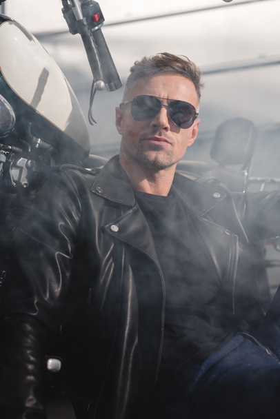 classic motorbiker in black sunglasses by motorbike in garage - 写真・画像