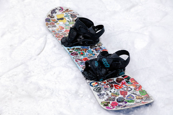 Rusia, Sheregesh 2018.11.18 Primeros planos de snowboard adornado con pegatinas de colores sobre nieve blanca. Concepto de recreación después de montar, apres ski
 - Foto, Imagen