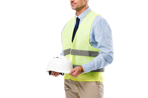 oříznutý pohled inženýra v bezpečnostní vesta drží helmu izolované na bílém - Fotografie, Obrázek