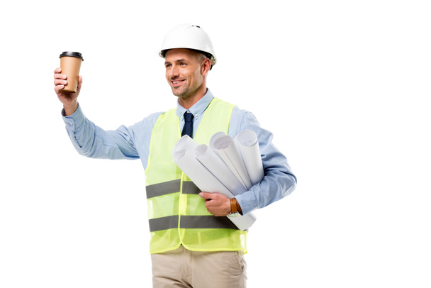 smiling engineer in safety vest holding blueprints and coffee to go isolated on white - Foto, Imagem
