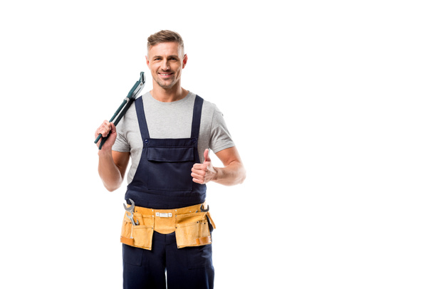 smiling plumber holding pipe wrench and showing thumb up sign isolated on white - Zdjęcie, obraz