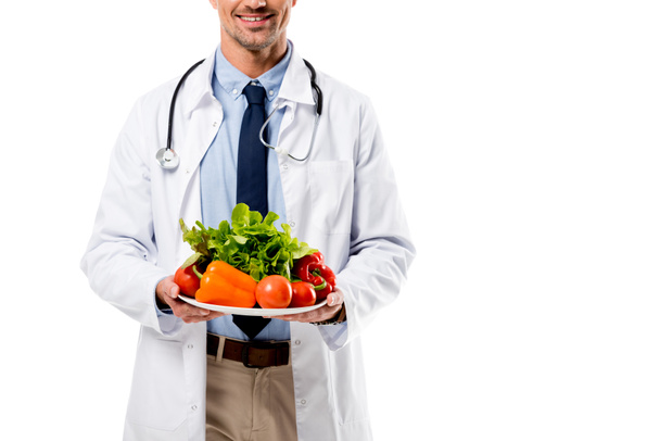 vue recadrée du médecin tenant assiette de légumes frais avec verdure isolé sur blanc, concept de saine alimentation
 - Photo, image