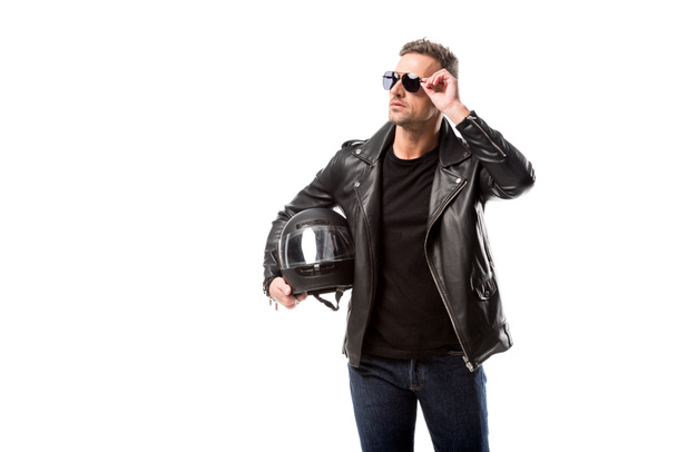 man in leather jacket and sunglasses holding motorcycle helmet and posing isolated on white - Foto, Bild