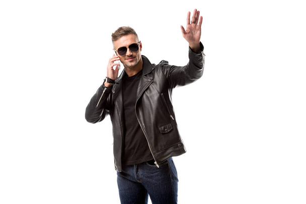 handsome man in sunglasses talking on smartphone, waving to someone and looking away isolated on white - Foto, afbeelding