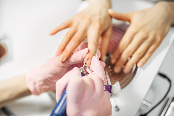 Esthéticienne en gants polissage des ongles de cliente, vue de dessus, manucure en salon de beauté. Manucure faisant soin des mains procédure cosmétique
 - Photo, image