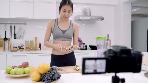 Blogger sporty Asian woman using camera recording how to make avocado juice video for her subscriber, female use organic fruit making avocado juice by herself at home. Healthy food concept. - Footage, Video