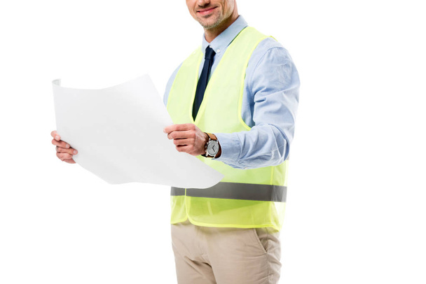 περικοπεί άποψη της χαμογελώντας μηχανικός στην ασφάλεια vest κρατώντας blueprint απομονωθεί σε λευκό - Φωτογραφία, εικόνα
