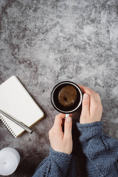 Hand holds  cup of coffee on gray table with candle, notebook, pen .Winter  concept. Flat lay, top view. - Foto, afbeelding