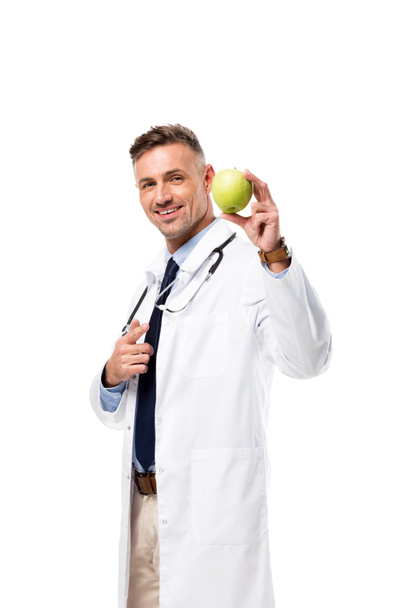 smiling doctor pointing with finger at green apple isolated on white, healthy eating concept - Foto, immagini