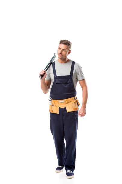 ernstige loodgieter in overalls houden pipe wrench geïsoleerd op wit - Foto, afbeelding