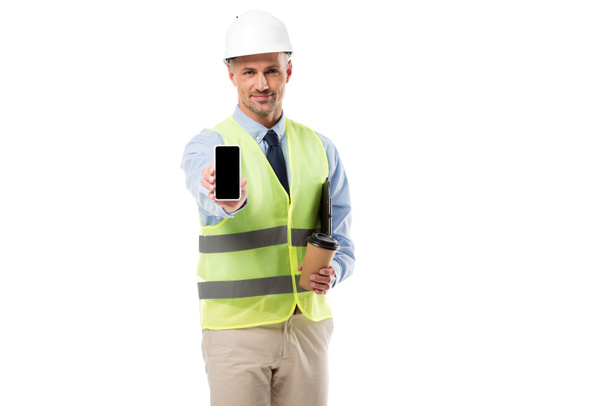 Ingeniero guapo sosteniendo teléfono inteligente con pantalla en blanco y café para ir aislado en blanco
 - Foto, Imagen