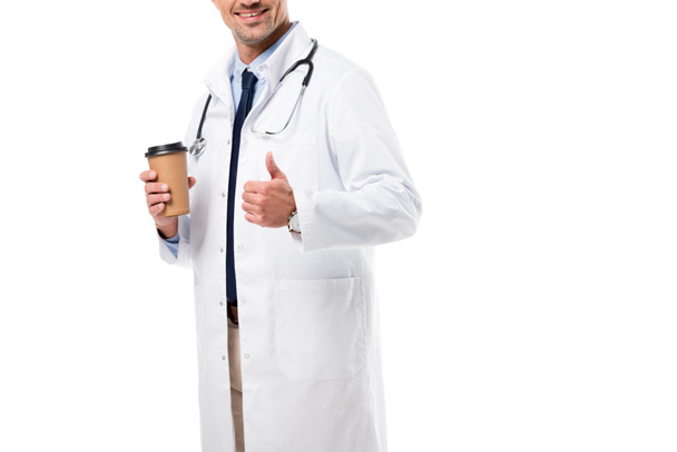 обрезанный вид улыбающийся доктор держит кофе идти и делает большой палец вверх знак изолирован на белом
 - Фото, изображение