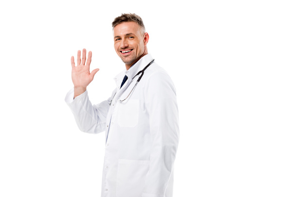 handsome doctor waving and looking at camera isolated on white  - Fotó, kép