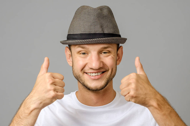 Portrait of man smiling and showing two thumbs up on gray background - Fotografie, Obrázek