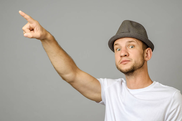 Portrait of suspicious man pointing left with hand and looking at camera on gray background - Foto, Bild