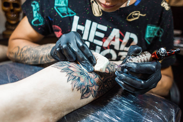 The tattoo artist creates a picture on the body of a man. close-up of tattoo machines and hands - 写真・画像
