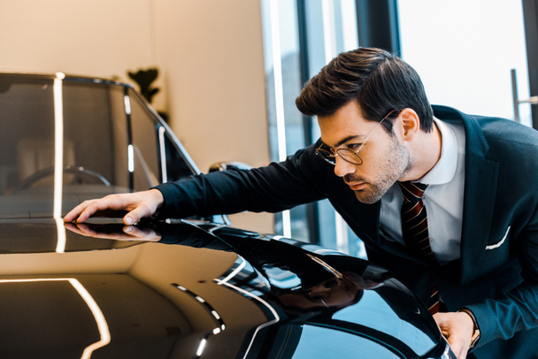 focused businessman in eyeglasses choosing automobile in dealership salon - Foto, Bild