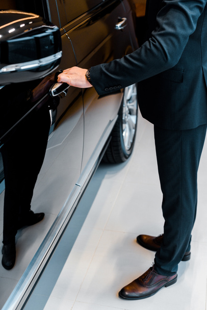 cropped image of businessman in suit opening door of black automobile - Foto, Imagen