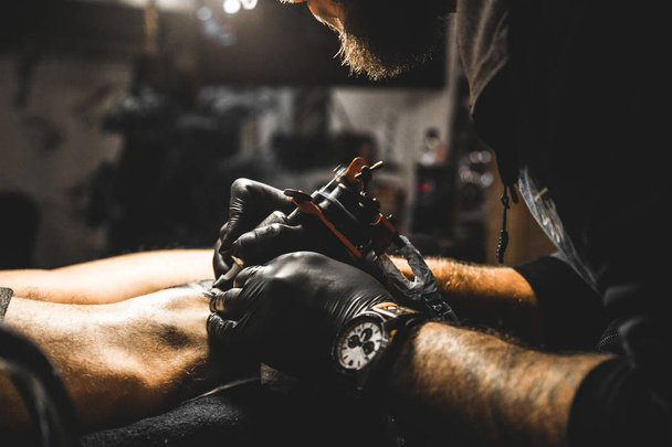 The tattoo artist creates a picture on the body of a man. close-up of tattoo machines and hands - Foto, Bild