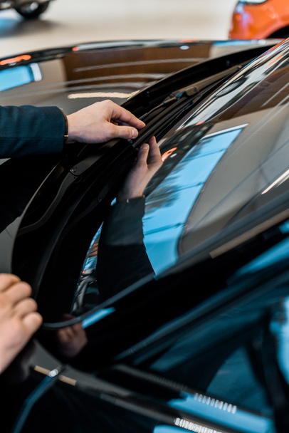 cropped image of businessman adjusting windshield wipers of black automobile  - Zdjęcie, obraz