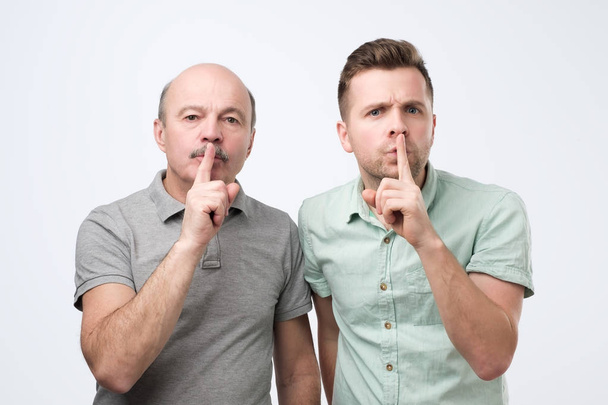 Dos hombres maduros mantienen el dedo en los labios, trata de mantener la conspiración
 - Foto, imagen