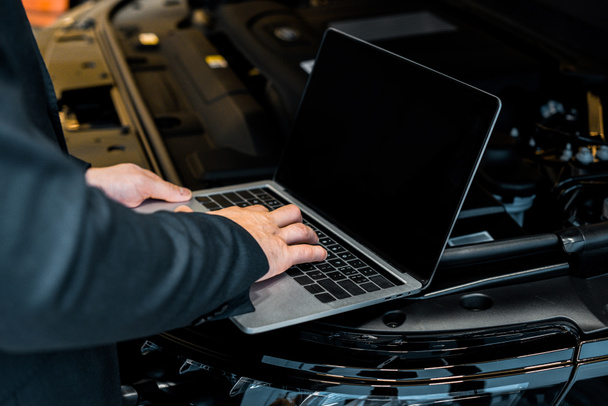 partial view of businessman checking car hood with laptop with blank screen   - Photo, Image