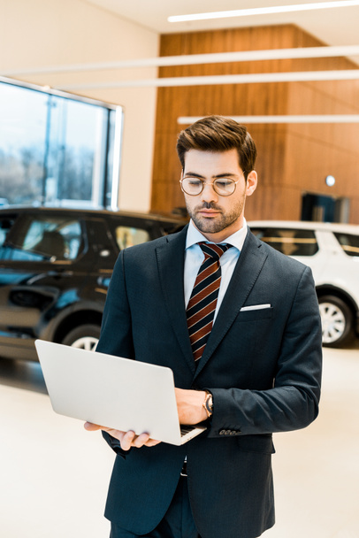 selective focus of businessman in formal suit using laptop at dealership salon - 写真・画像