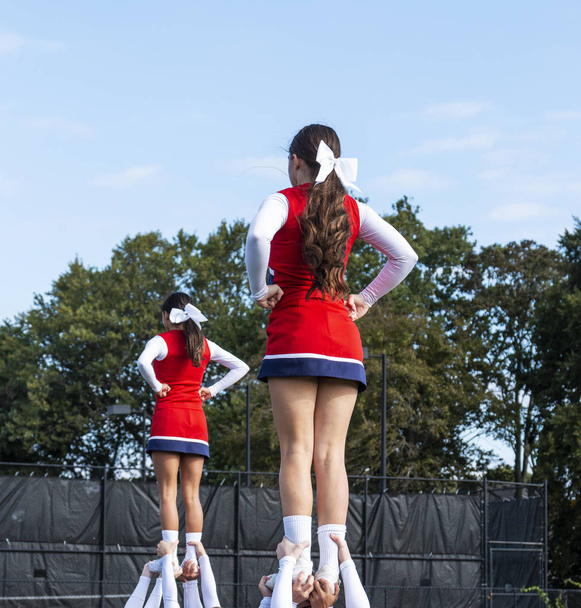 Deux escouades de pom-pom girls du lycée tenant leur coéquipier par les chevilles pendant une routine
. - Photo, image