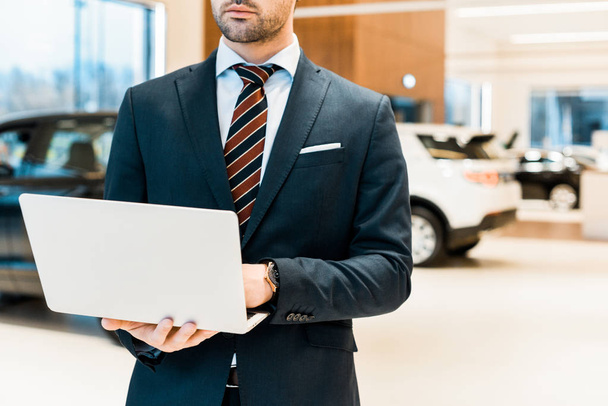 partial view of businessman in formal suit using laptop at dealership salon - 写真・画像