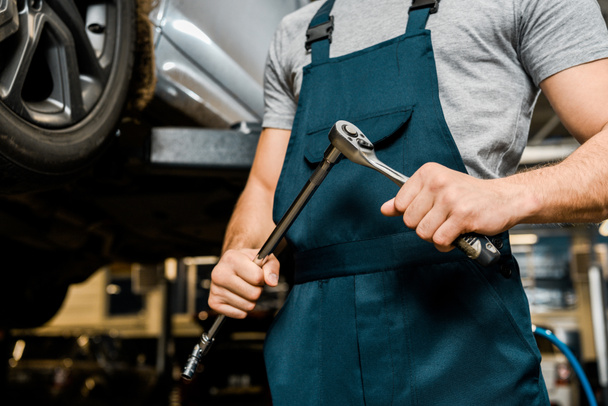 cropped shot of auto mechanic with lug wrench in hands at mechanic shop - Foto, imagen