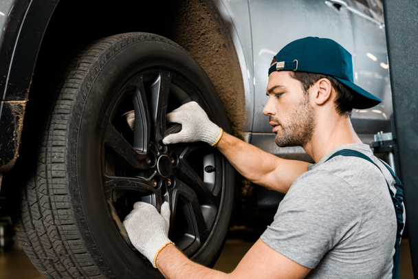 side view of auto mechanic in protective gloves checking automobile wheel at auto repair shop - Fotoğraf, Görsel
