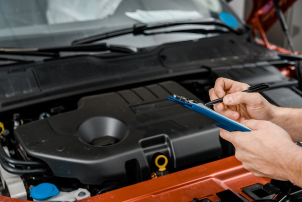 cropped shot of repairman with notepad examining car at auto repair shop - Foto, imagen