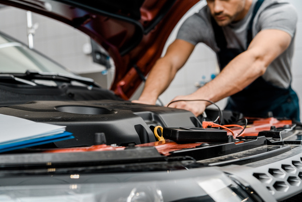 Schnappschuss von Automechaniker mit Multimeter-Voltmeter zur Überprüfung der Autobatteriespannung im Mechanikerladen - Foto, Bild