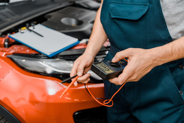cropped shot of auto mechanic holding multimeter voltmeter for car battery voltage checking at mechanic shop - Photo, Image