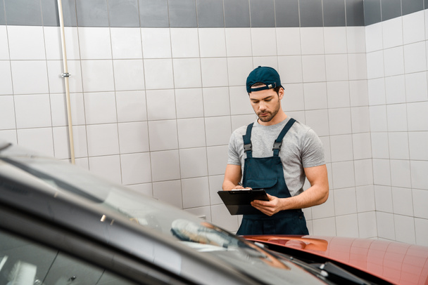 portrait of auto mechanic with notepad examining car at auto repair shop - Photo, Image