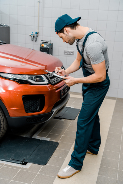 auto mechanic with notepad examining car at auto repair shop - Photo, Image