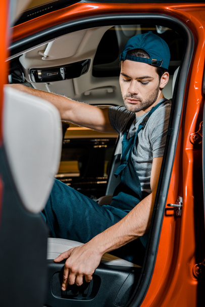 side view of auto mechanic sitting on drivers seat in car - Foto, Imagen