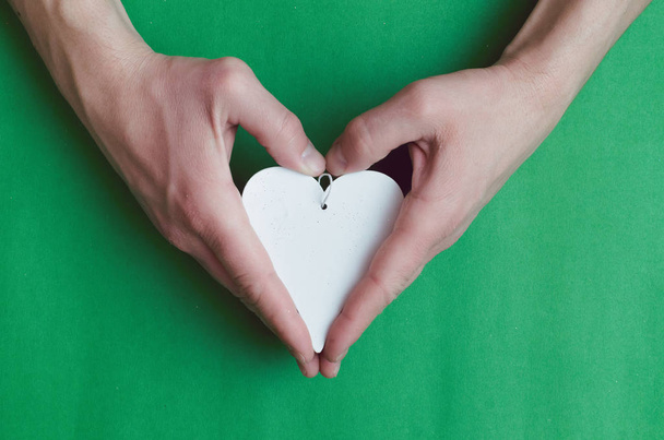 Male hands holding a white heart shape gift over green background. - Foto, imagen