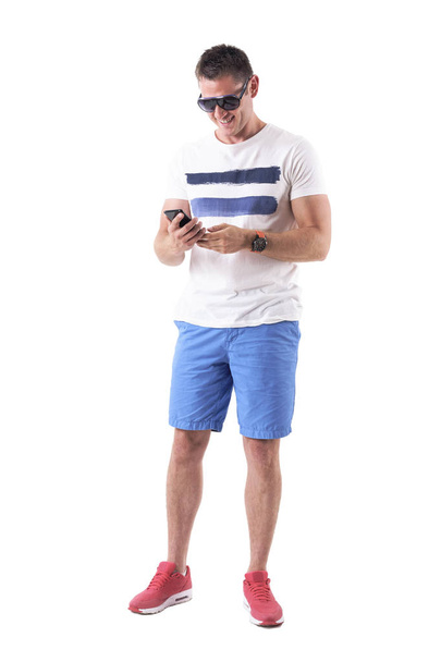 lächelnder entspannter glücklicher Mann mit Handy in Sommerkleidung. Ganzkörper isoliert auf weißem Hintergrund.  - Foto, Bild