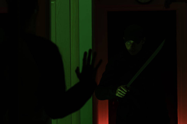Picture of thief with machete and man with hands up in dark room - Foto, immagini