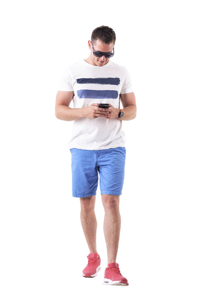 Young past man in casual zomer kleding lopen en het gebruik van de mobiele telefoon. Volledige lichaam geïsoleerd op witte achtergrond.  - Foto, afbeelding