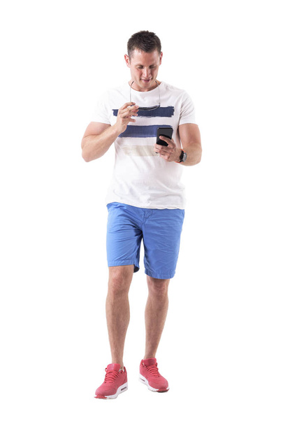 Hombre feliz caminando y leyendo mensajes en el teléfono móvil o navegando por la red. Cuerpo completo aislado sobre fondo blanco
.  - Foto, imagen